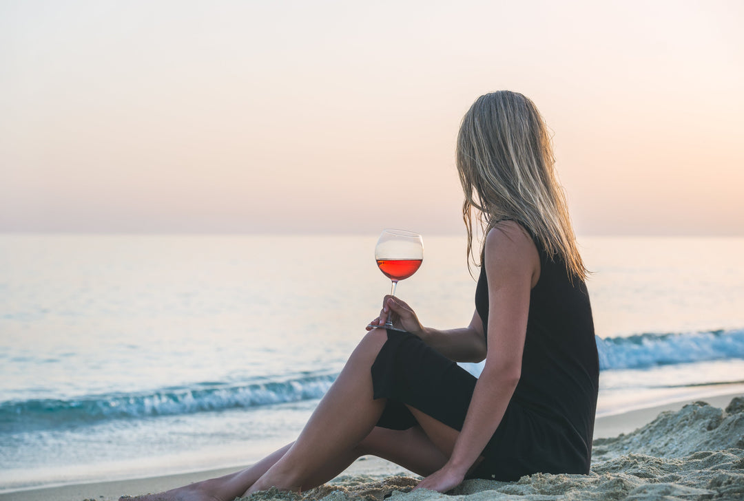 Woman enjoying biodynamic wines Italy at the beach during sunset with a glass of red wine.